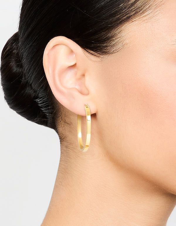 Featuring waterproof medium flat hoop earrings in gold plated stainless steel worn on ear view