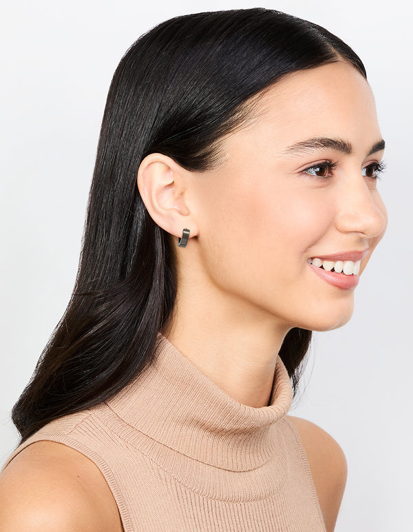 Crafted from waterproof black coated stainless steel wide huggie earrings on model view