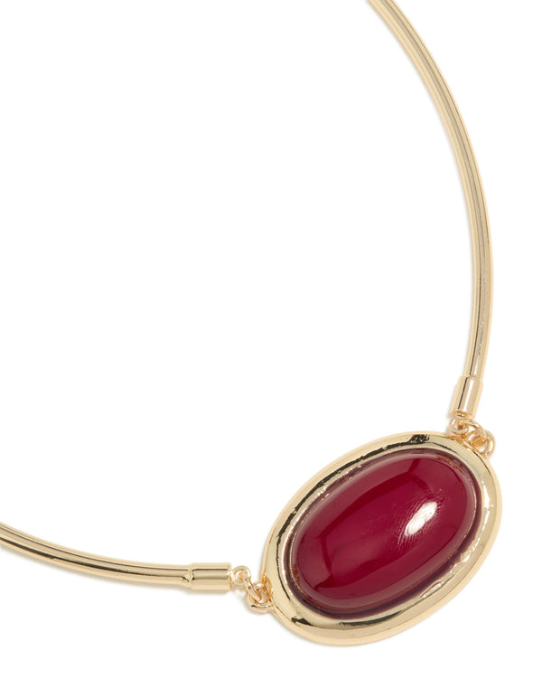 Showcasing a gold necklace with red large stone and tube elements in crimson close up view