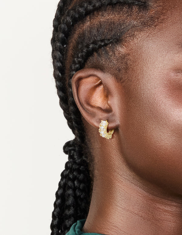 Crafted from gold plated materials, these cubic zirconia oval huggie earrings feature a stunning design in clear and gold on ear view