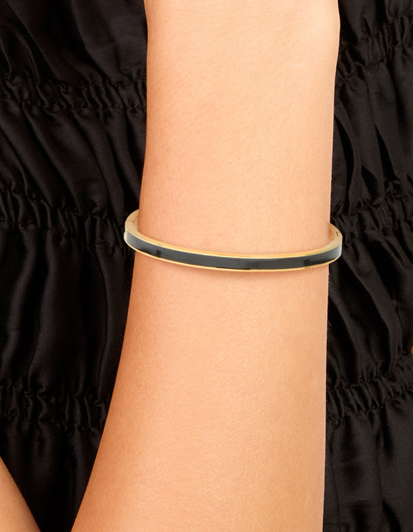 Showcasing a waterproof hinged bangle made of gold plated stainless steel with thick black enamel in a dainty design on wrist view