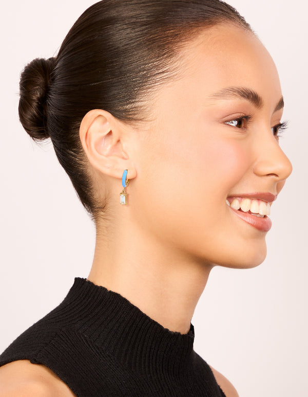 Designed with waterproof stainless steel huggie earrings in sky blue enamel, featuring cubic zirconia charm on model view