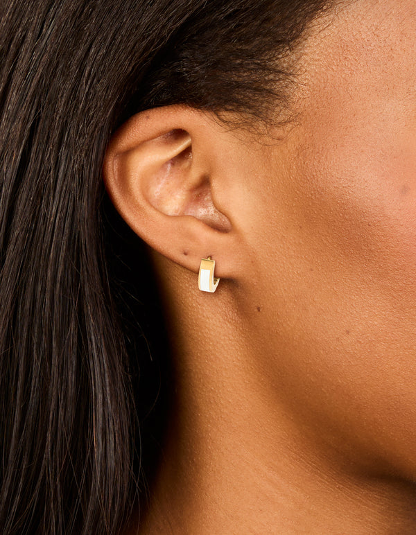 Featuring waterproof gold plated stainless steel small white enamel inlay huggie earrings on ear view