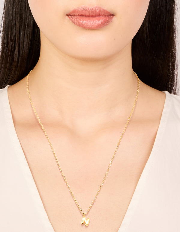 Featuring a waterproof bubble letter N initial pendant necklace in gold plated stainless steel on neck view
