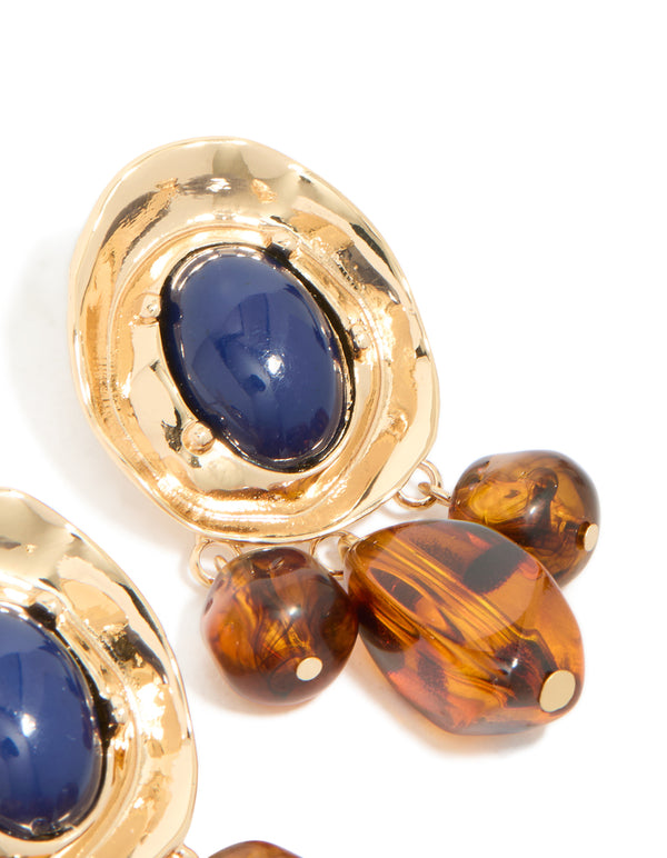 Highlighting statement charm and beaded medallion drop earrings in gold with midnight blue acrylic and saddle brown details close up view