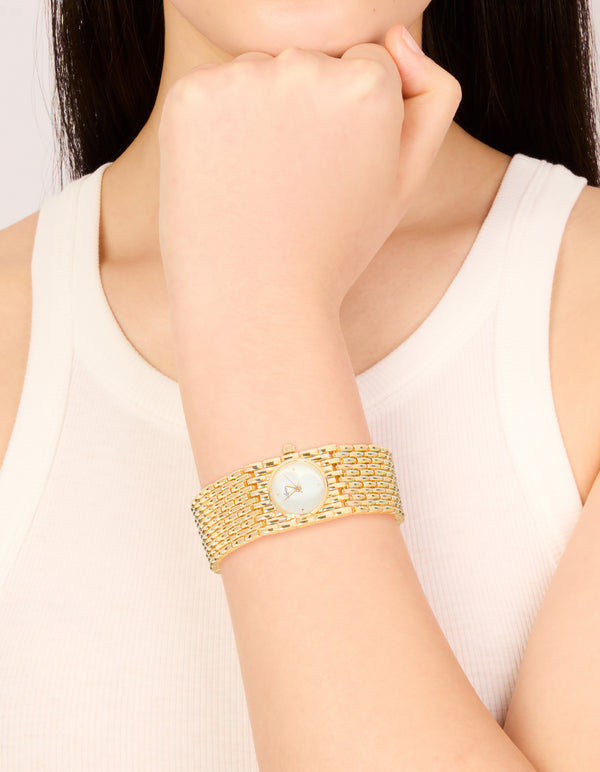 Showcasing a women's chunky statement bracelet watch with white dial look with stone, round shape, analog display, link band in gold, and casual occasion styling on wrist view