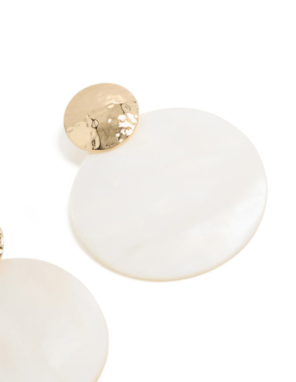 Close up of hammered gold texture and white genuine shell disc in statement ocean-inspired drop earrings close up view