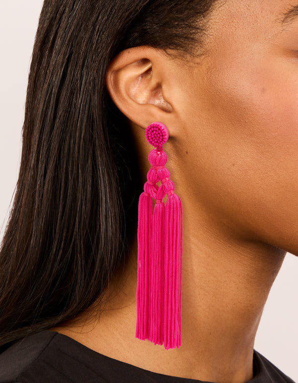 Featuring statement hot pink fabric tassel drop earrings with beads worn elegantly on ear view