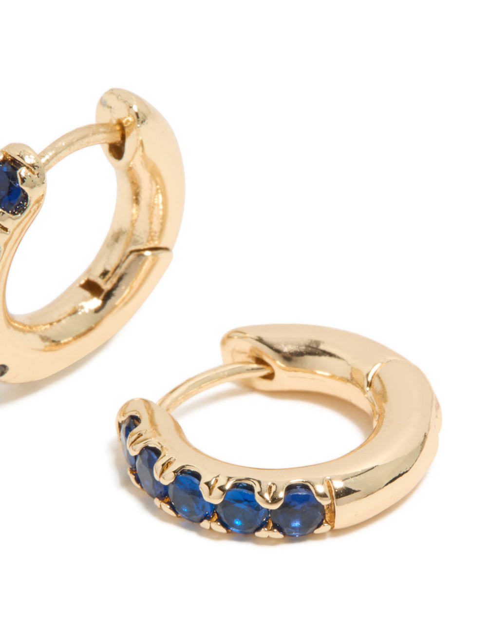 Small huggie clicker earrings with cubic zirconia in gold and dark blue highlighting closure mechanism in a post detail view