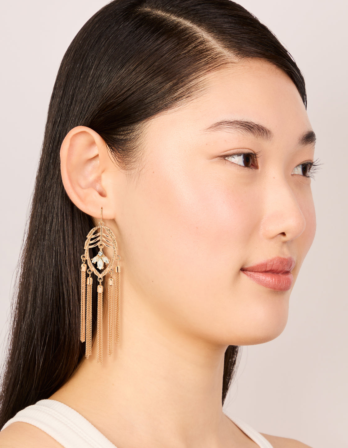 Featuring statement charm tassel drop earrings in gold with leaf and clear diamante details on model view