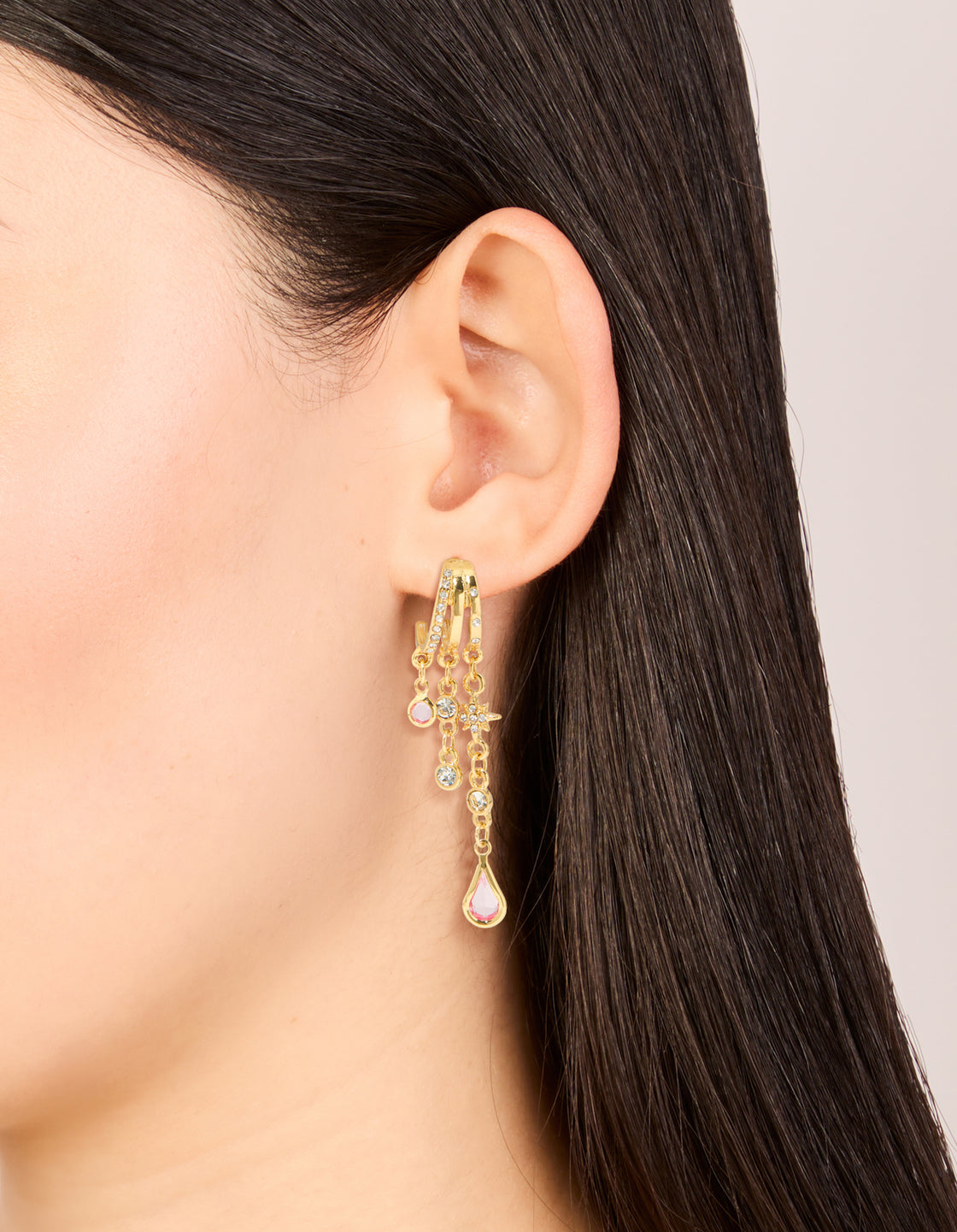 Highlighting gold plated pink cubic zirconia chain drop earrings with star and celestial charm details in statement style on ear view