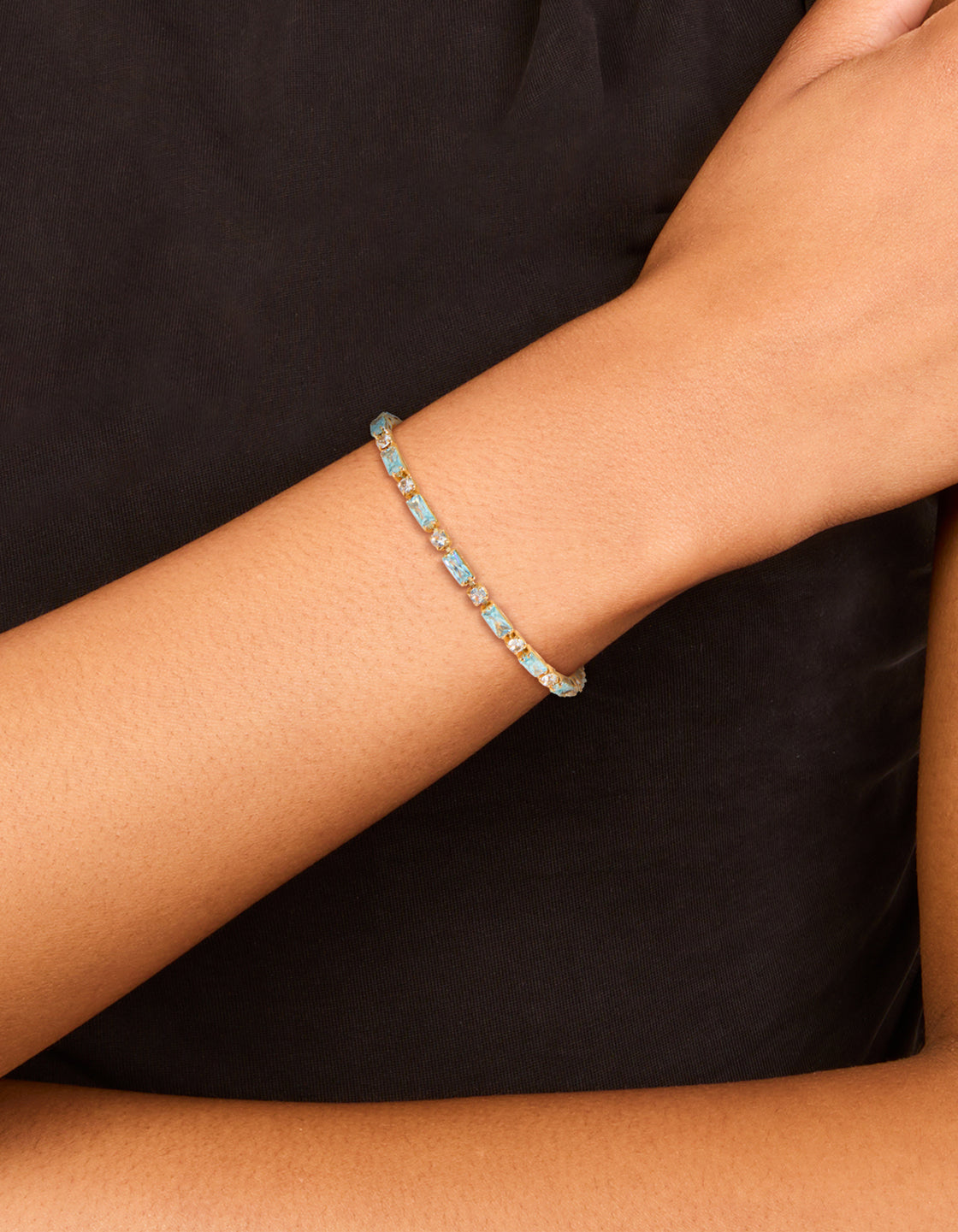 Crafted from gold plated materials, this clear and blue baguette cut cubic zirconia toggle bracelet is shown on wrist view