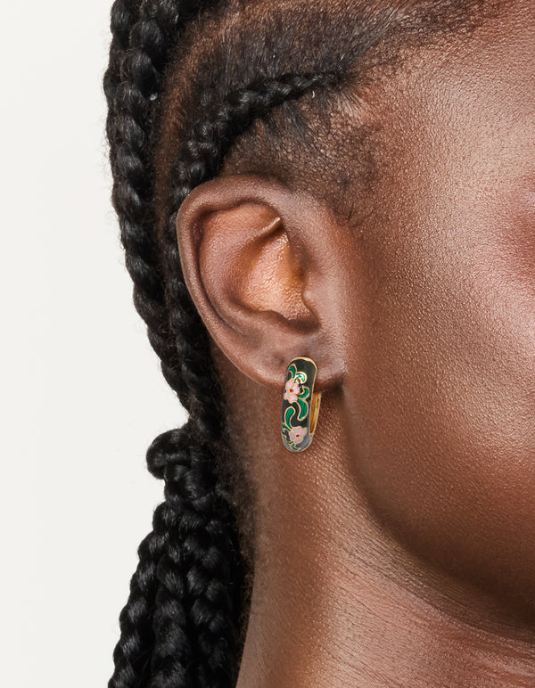 Showcasing thick huggie earrings with floral pattern in enamel, statement style, gold and black with pink accents on ear view