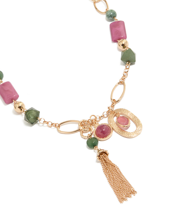 Showcasing a gold pink and green acrylic beaded long fringe necklace with charm tassel in statement style close up view