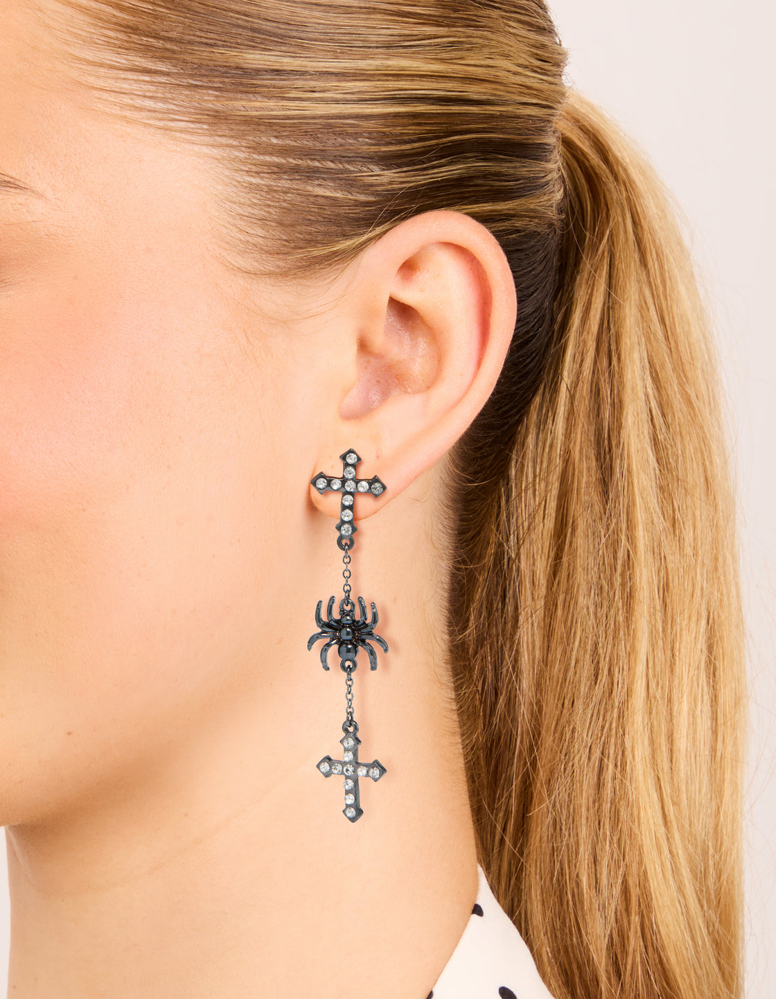 Crafted from gunmetal silver, these statement drop earrings featuring spider and cross charms on ear view