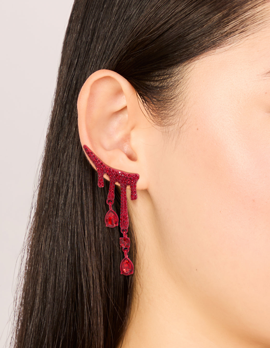Displaying red coated metal blood droplet drop earrings with statement charm and glitter on ear view