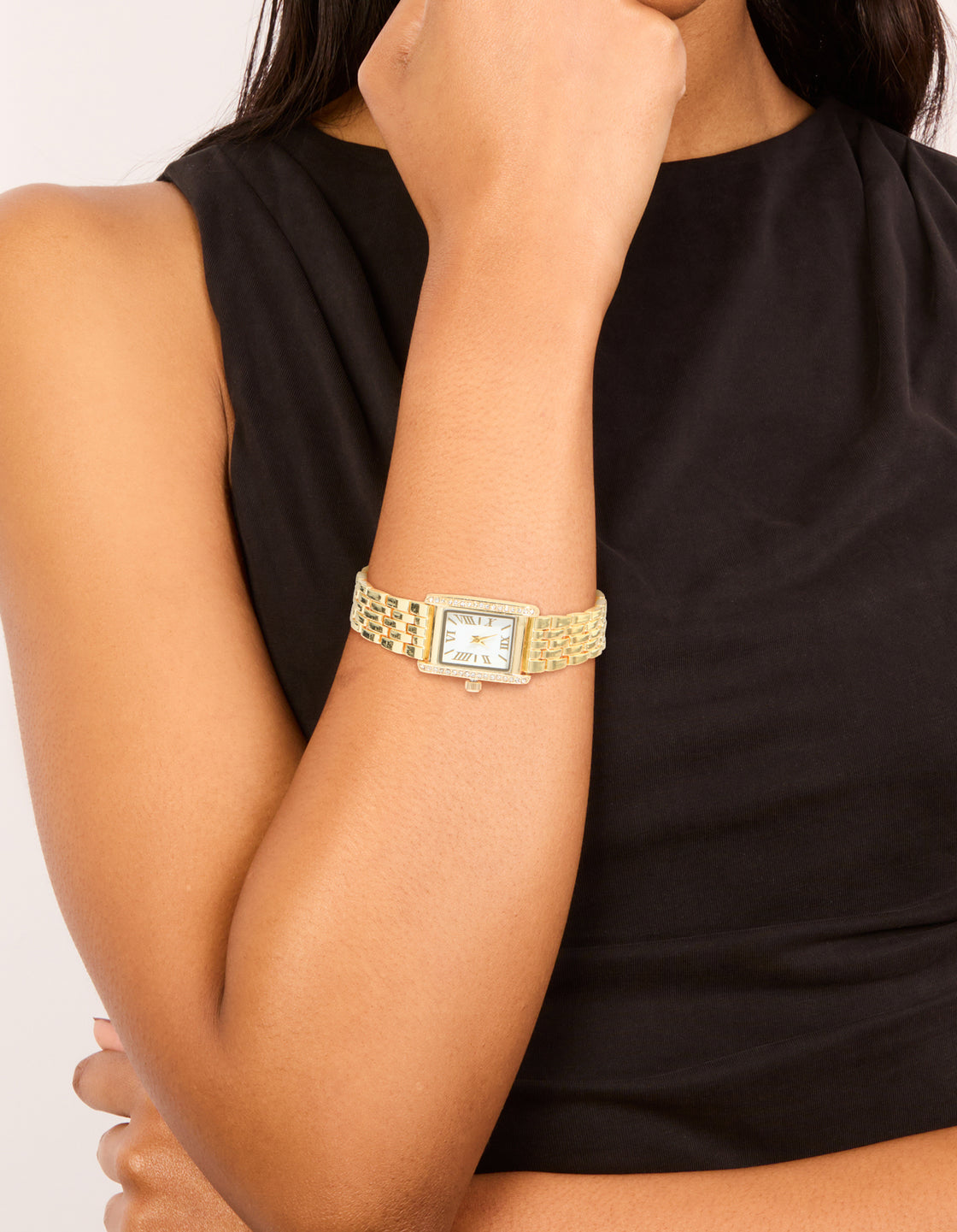 Showcasing a gold and diamante Roman numeral watch featuring a white dial, rectangular shape, link band strap, analog type designed for women's formal occasions on wrist view