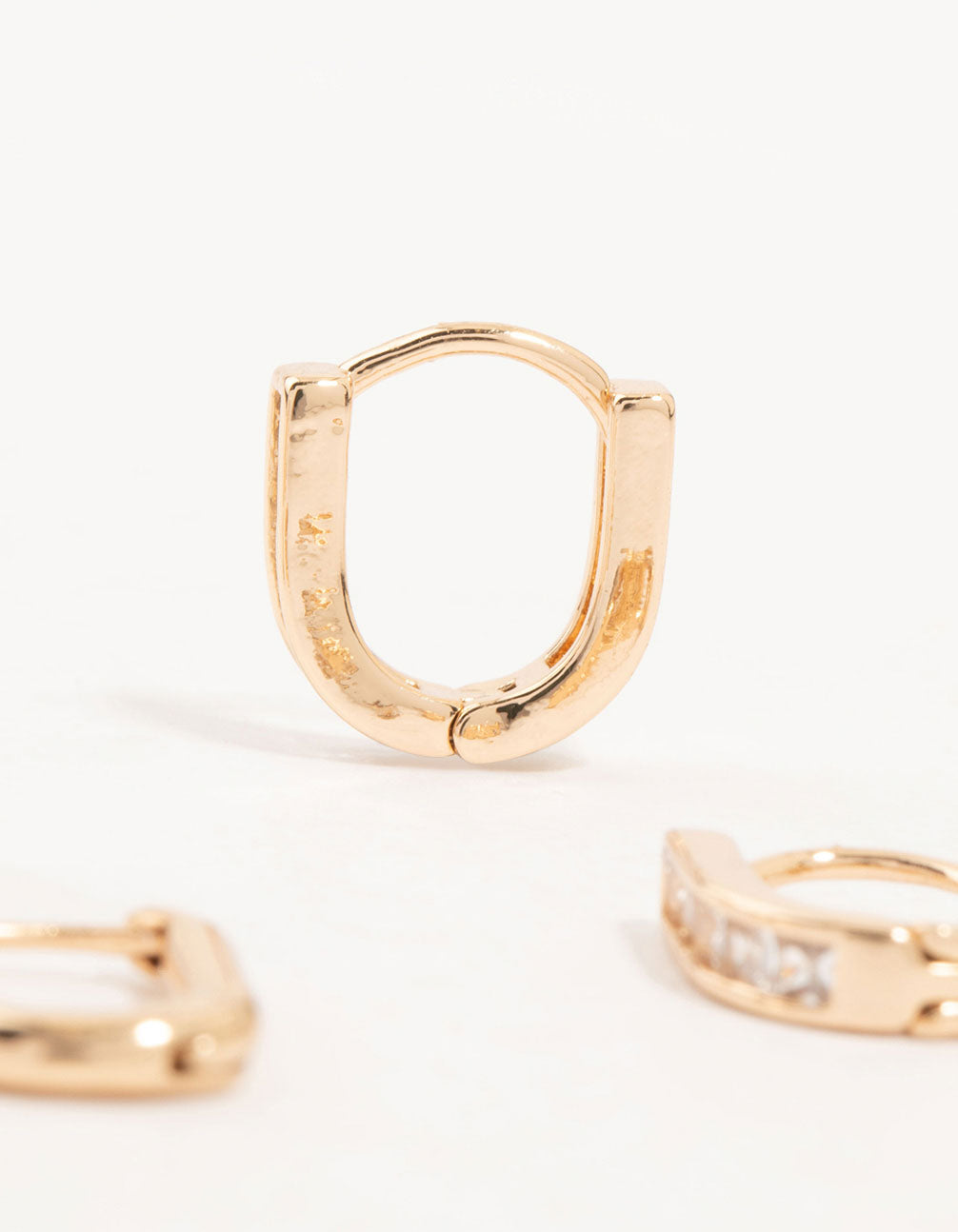 Presenting gold cubic zirconia oval huggie earrings in a 3-pack showcasing stone setting and closure detail view