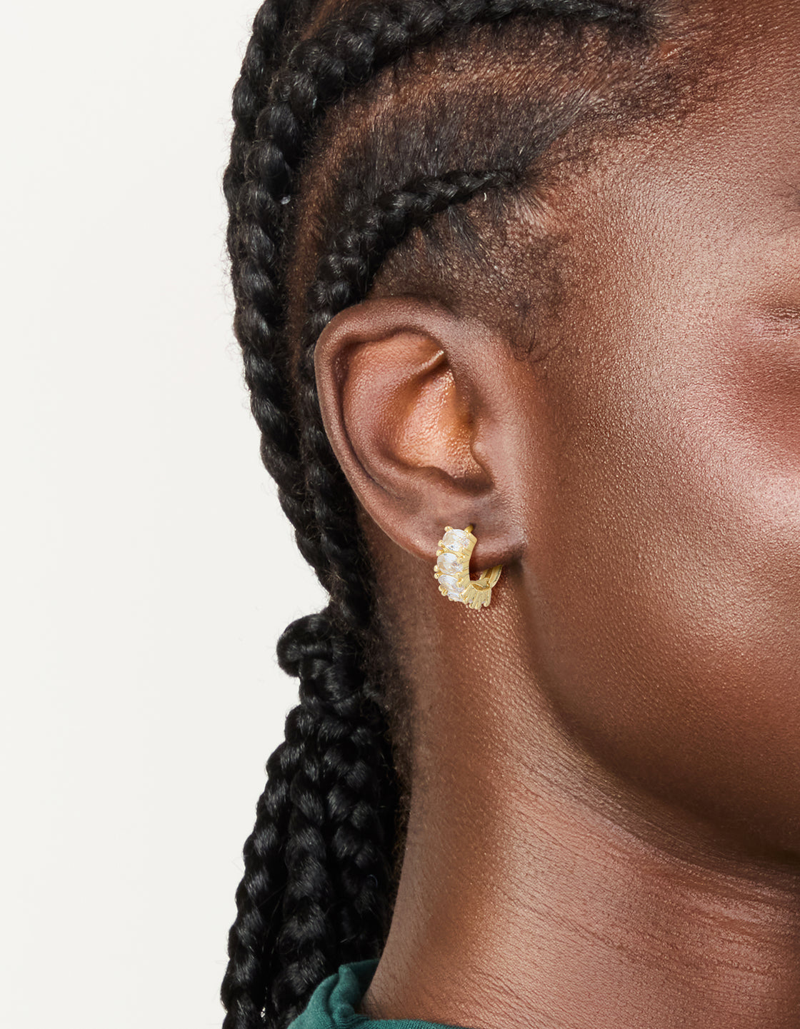 Crafted from gold plated materials, these cubic zirconia oval huggie earrings feature a stunning design in clear and gold on ear view