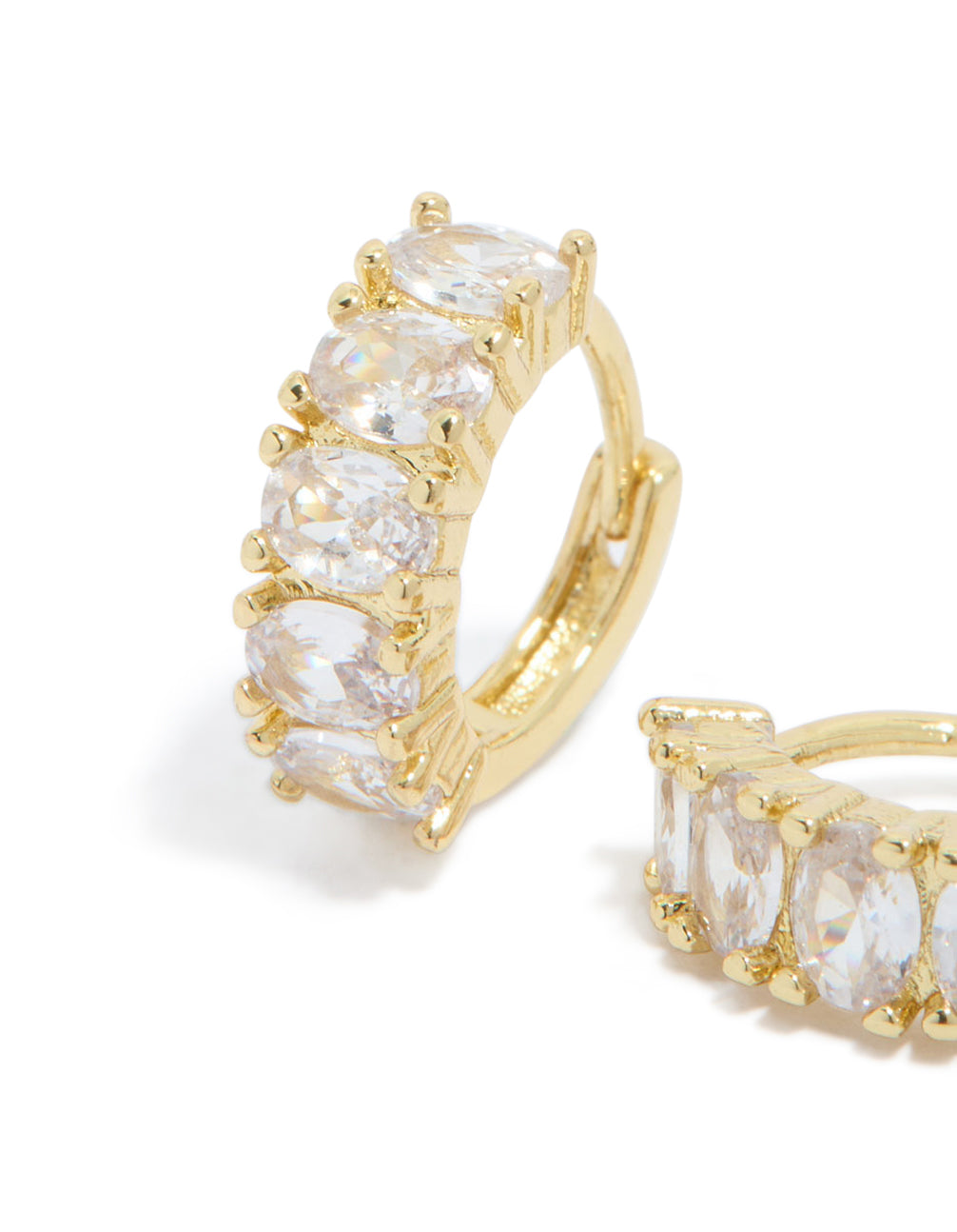 Featuring gold plated cubic zirconia oval huggie earrings with detailed prong settings in clear and gold close up view