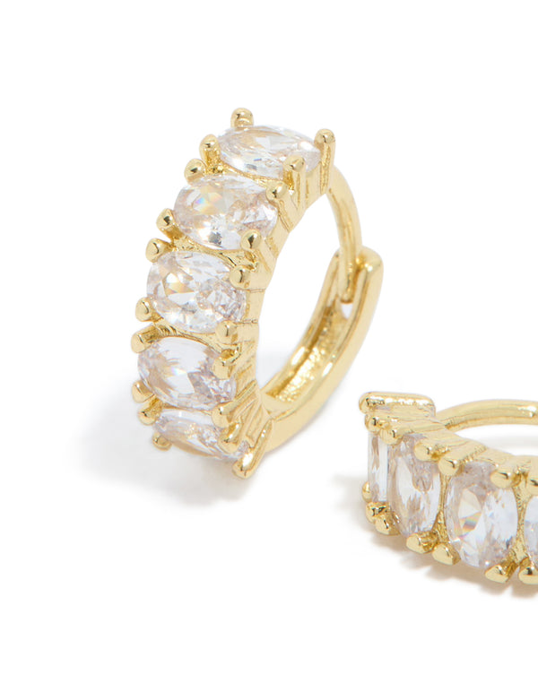 Featuring gold plated cubic zirconia oval huggie earrings with detailed prong settings in clear and gold close up view