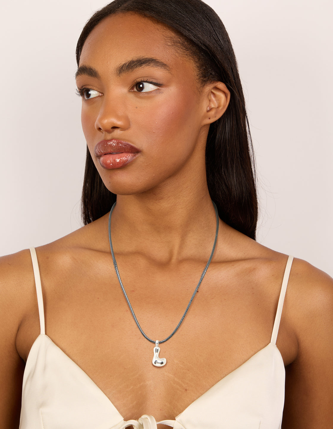 Designed with a waterproof stainless steel large bubble letter L initial pendant on grey cord necklace on model view
