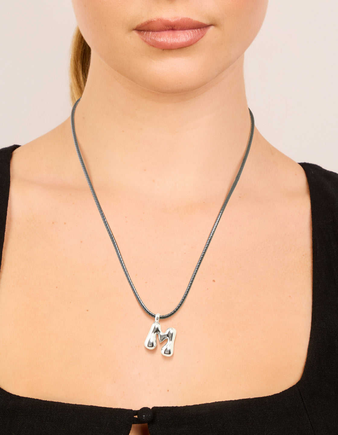 Featuring a waterproof stainless steel large bubble letter M initial pendant with grey cord dainty style necklace on neck view