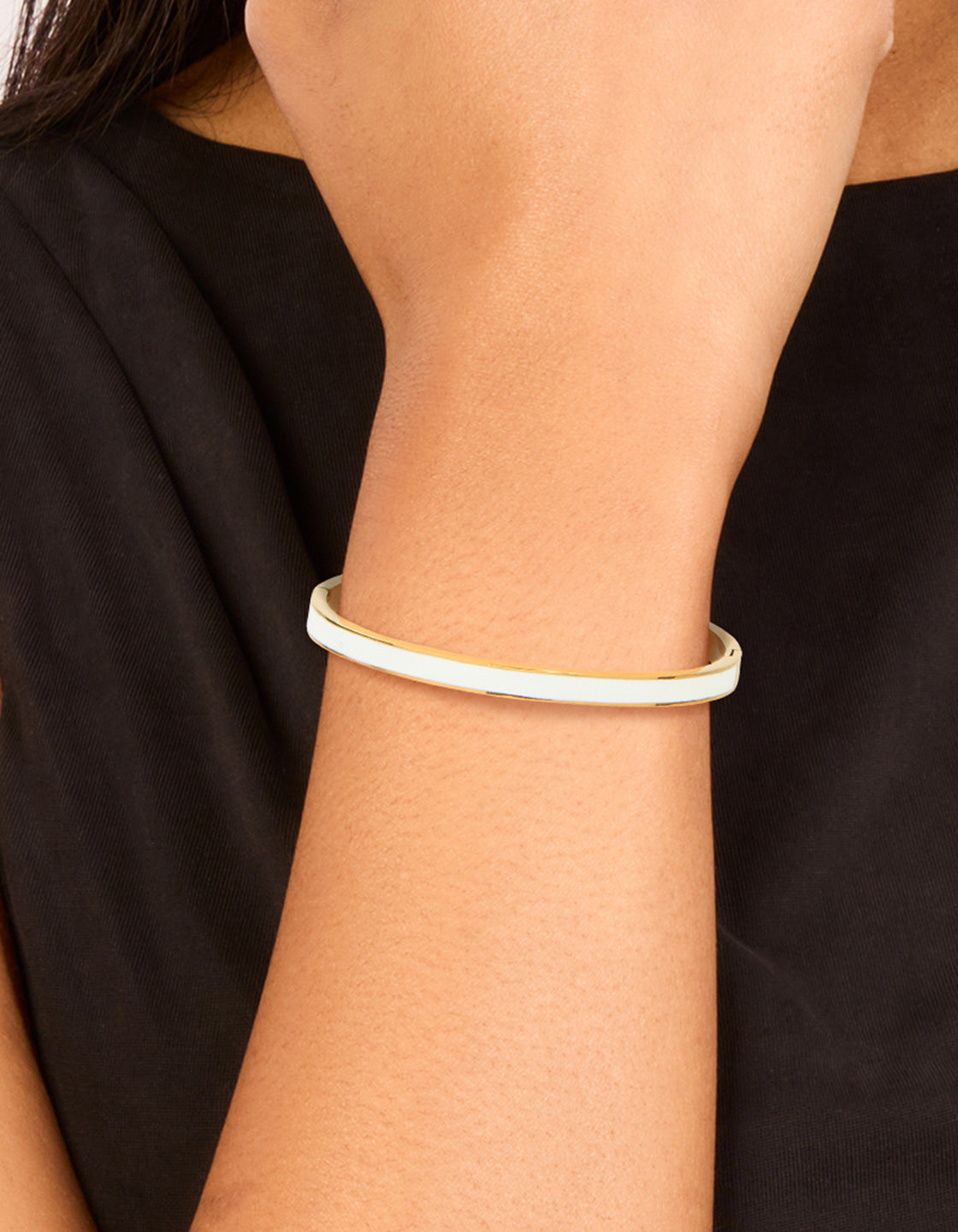 Featuring a waterproof gold plated stainless steel white enamel hinged bangle in dainty style on wrist view