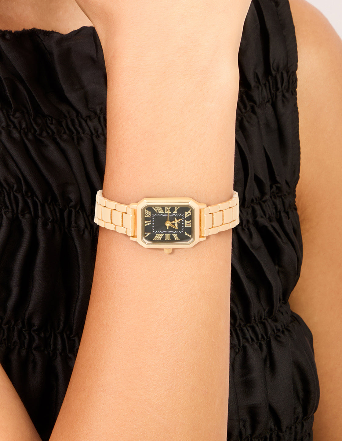 Showcasing a women's analog watch with black roman numeral rectangular dial, link band strap in gold, designed for formal occasions on wrist view