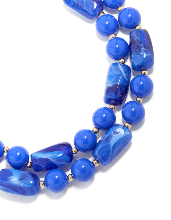 Showcasing a dark blue acrylic beaded long layered necklace with balls and statement style in royal and dodger blue with gold accents close up view