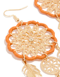 Showcasing gold orange yarn dreamcatcher feather drop earrings with statement charm close up view - link has visual effect only
