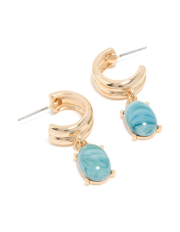Showcasing statement huggie hoop earrings in gold with blue acrylic drop charms front view