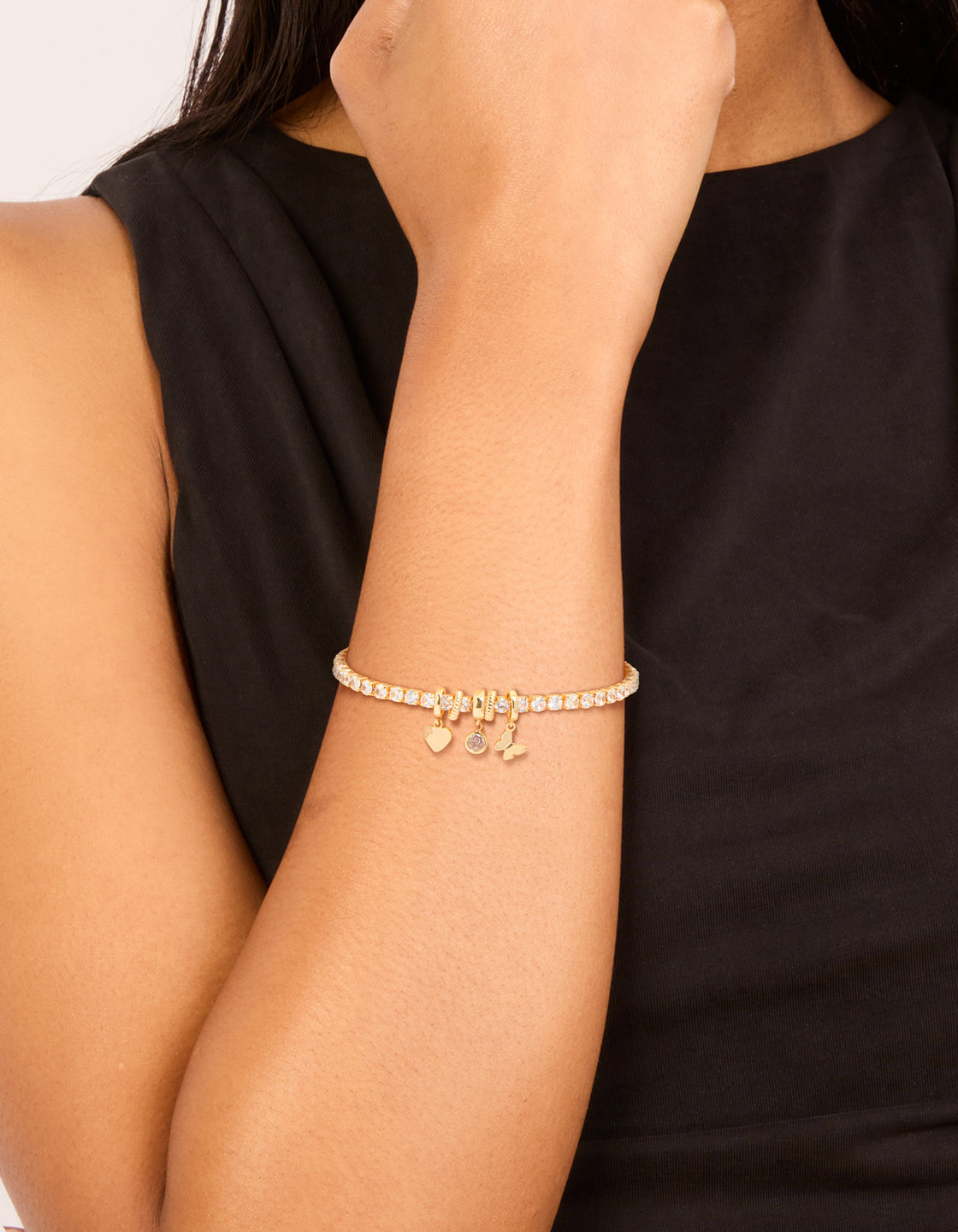 Showcasing a gold plated cubic zirconia mixed charm tennis bracelet with butterfly and heart on wrist view