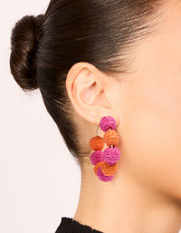 Showcasing statement hoop earrings with alternating light pink and coral paper-wrapped balls on ear view - link has visual effect only