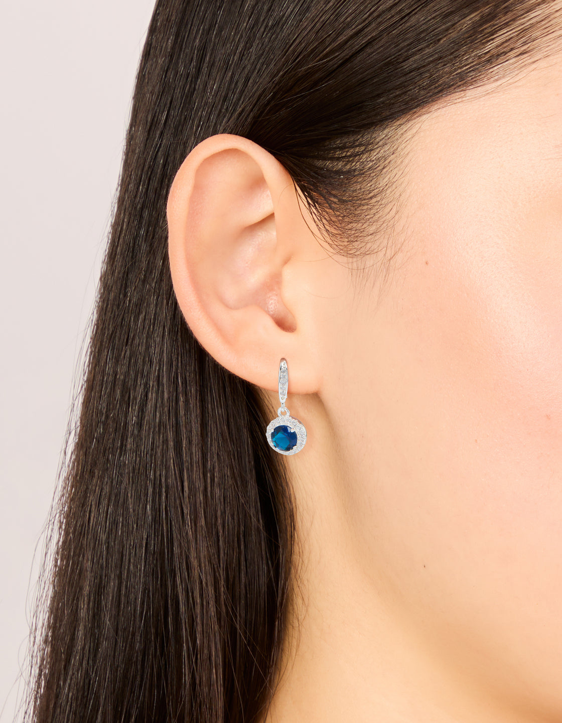 Beautifully crafted silver plated sapphire blue cubic zirconia halo drop earrings featuring navy stones on ear view