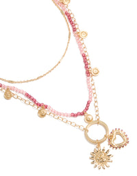 Showcasing a gold pink beaded and celestial layered necklace with charm featuring sun and heart in a statement design close up view - link has visual effect only