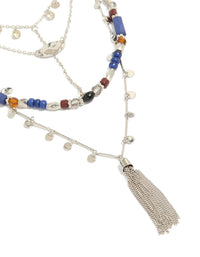 Showcasing a blue and brown beaded layered necklace featuring a tassel, charm disc, cubic zirconia, and crystal accents in silver, close up view - link has visual effect only