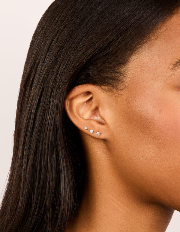 Showcasing sterling silver cubic zirconia starburst earrings in a dainty 3-pack with celestial and ball design, stud closure, and clear accents on ear view