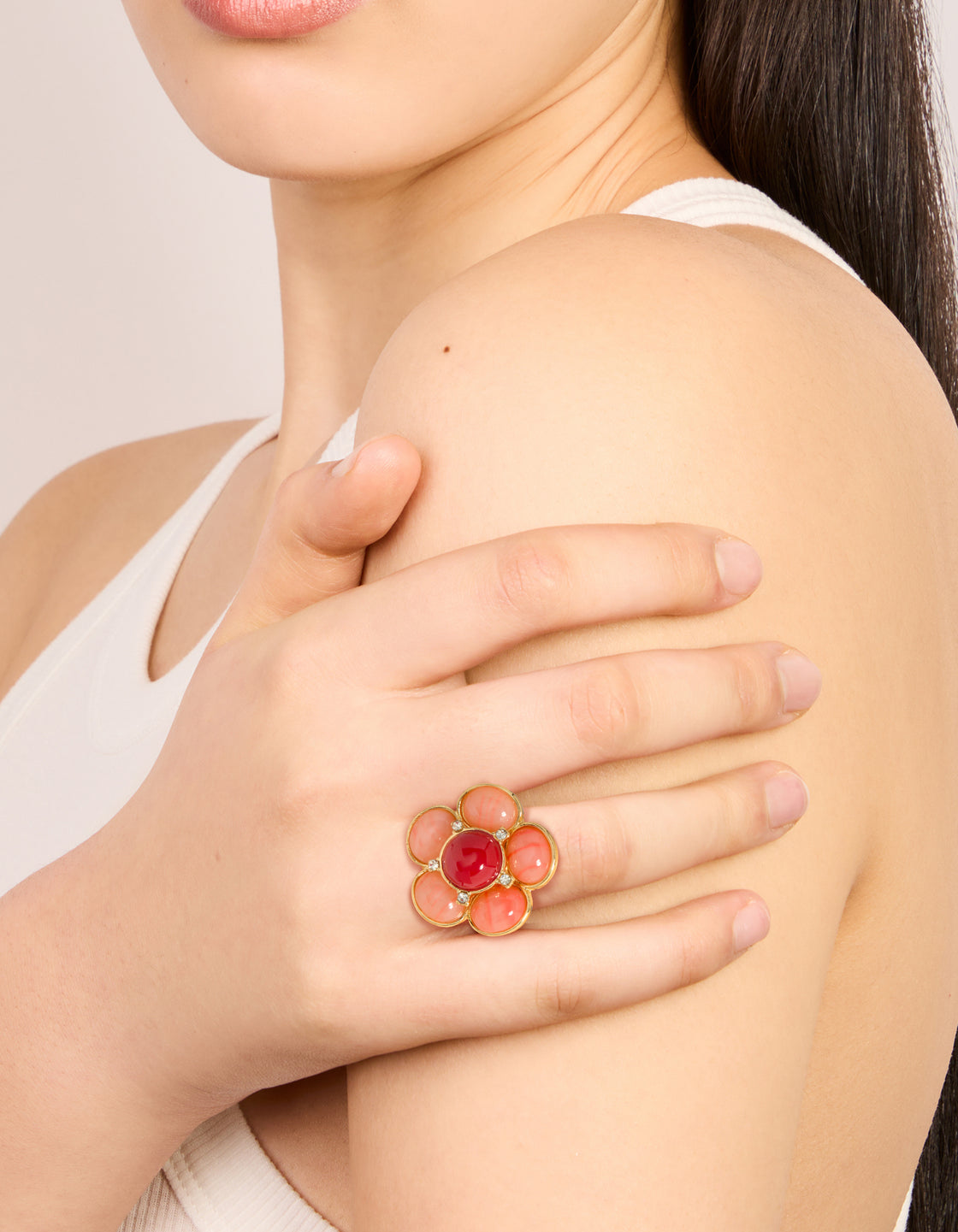 Elegant statement flower ring with gold plated material featuring pink stone in coral, crimson, and clear on finger view