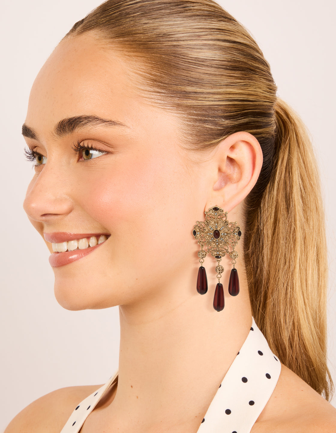 Crafted from gold with charm, and beads design statement drop earrings in maroon on model view