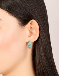 Crafted from enamel, these thick huggie earrings feature floral and leaf print in turquoise, gold, pink, and green with huggie closure on ear view - link has visual effect only