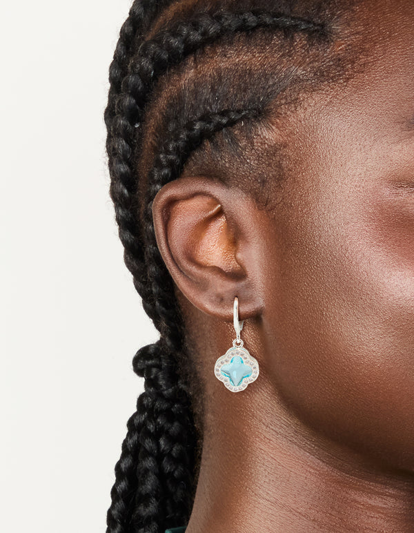 Featuring cubic zirconia, these blue and clear clover huggie earrings featuring floral in silver on ear view